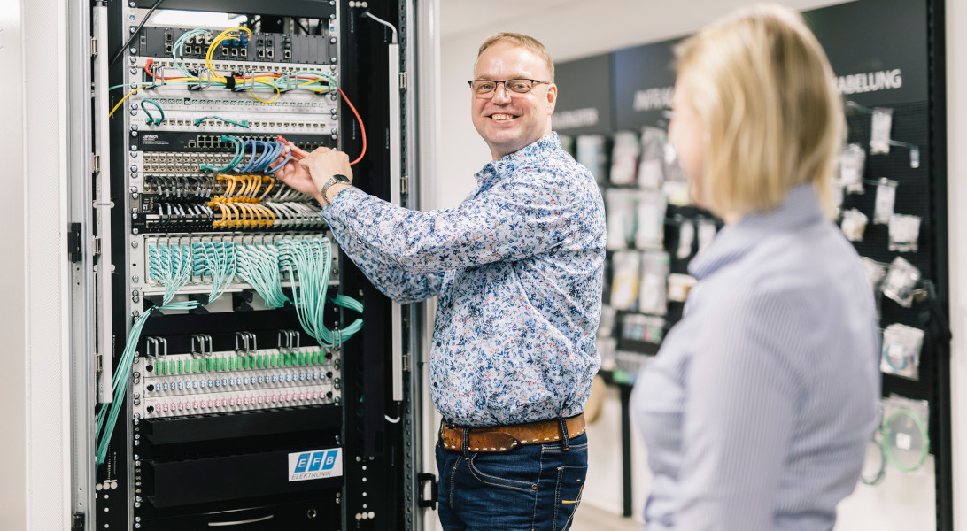 Produktmanager von EFB-Elektronik steht locker und freundlich an einem Serverschrank. Er ist im Gespräch mit einer Kollegin.